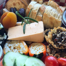 Load image into Gallery viewer, Close-up of plant-based cheeses, bread, crackers and vegetables in the Vegan Grazing Box.